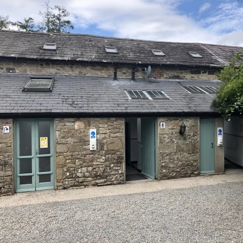 Single-storey stone buildings with blue-green doors on a gravel yard