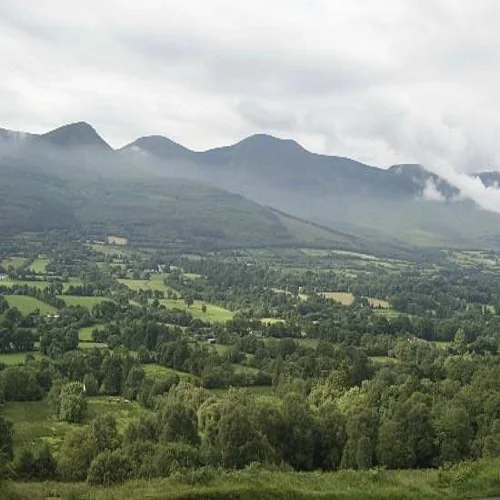 Green valley fields running up to a mountain ridge under cloud