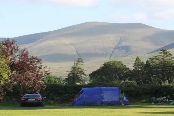 A blue tent on a grass field with a mountain behind