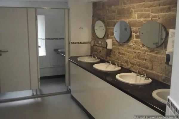 Washroom with a row of sinks and round mirrors on a stone wall